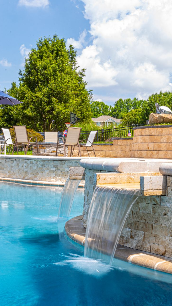 Pool with adjacent jacuzzi, surrounded by gray pavers. White elevated deck in background.