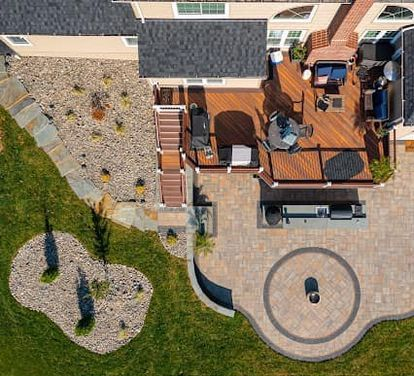 Aerial view of a home's backyard with a wooden deck, patio, landscaping, and outdoor furniture.