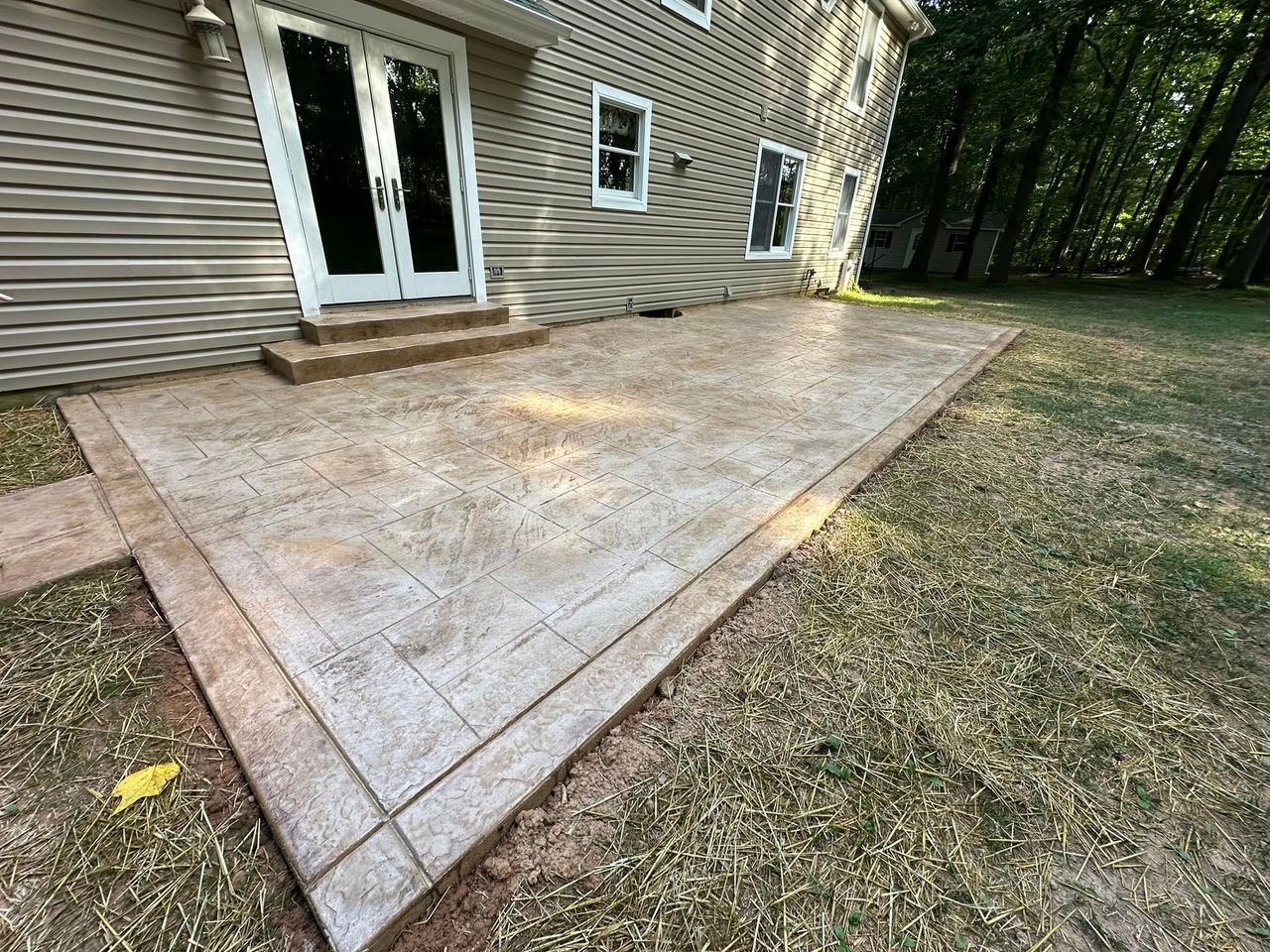 A concrete patio in front of a house in a backyard.