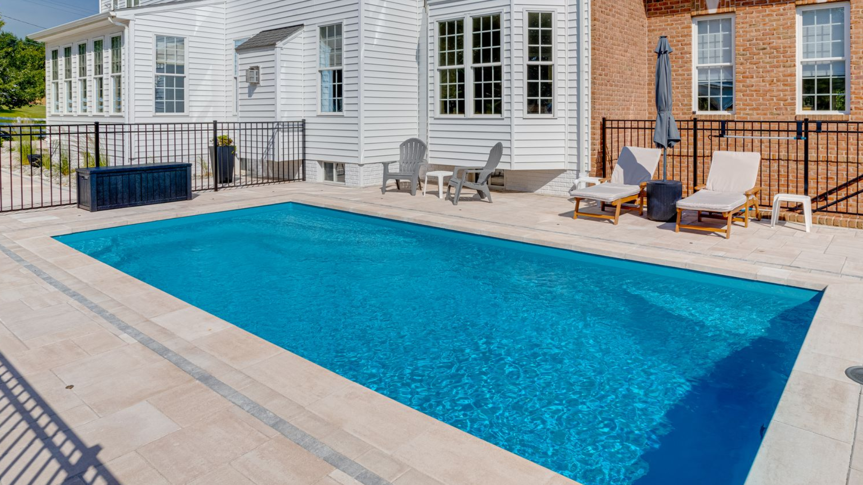 Swimming pool with lounge chairs, blue umbrellas, and lush greenery under a cloudy sky.