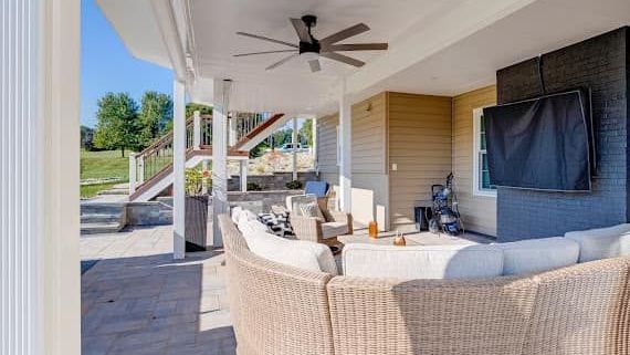 A living room with a couch , chairs , a television and a ceiling fan.