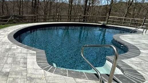 A large swimming pool with a staircase leading to it surrounded by trees.