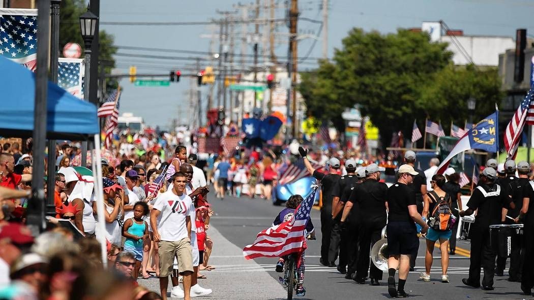 Families watching the Fourth of July parade on Frederick Road in Catonsville, Maryland, with flags and festive decorations.