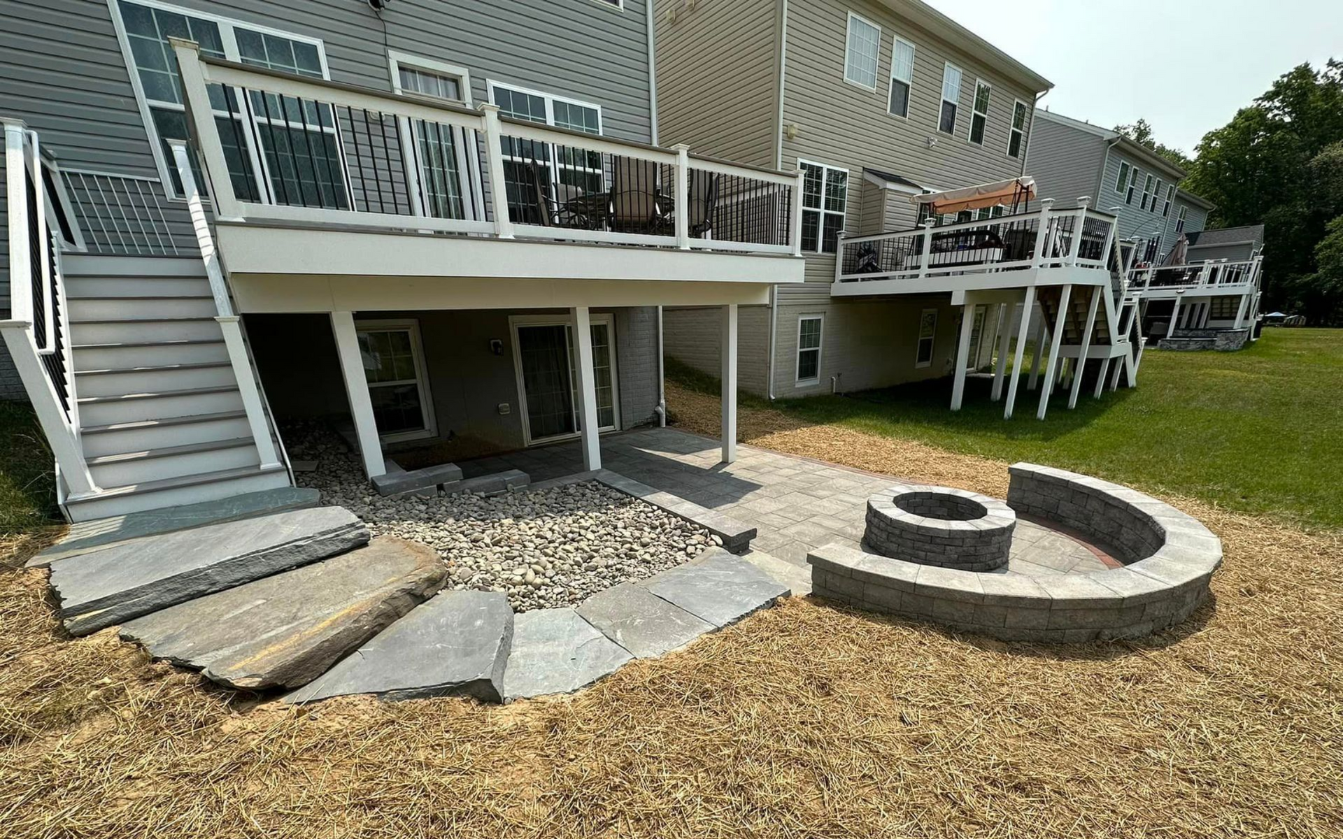 Backyard with a multi-level deck, stone patio, fire pit, and stairs leading down to a lower level.
