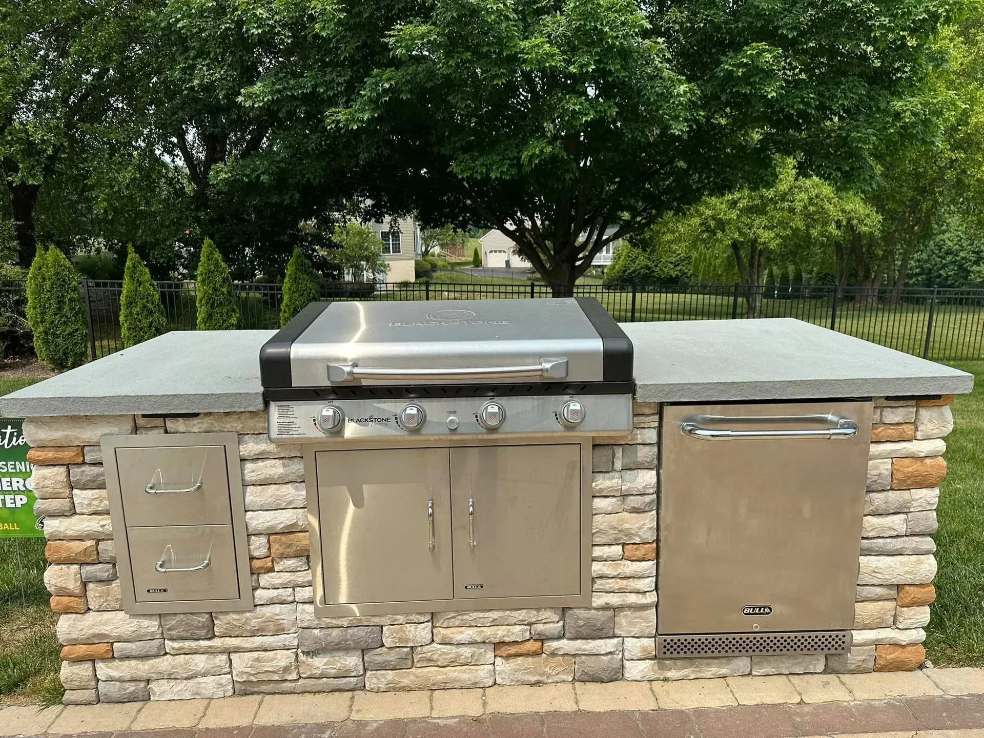Natural stone outdoor kitchen with built-in grill, refrigerator, and storage spaces in a Maryland backyard