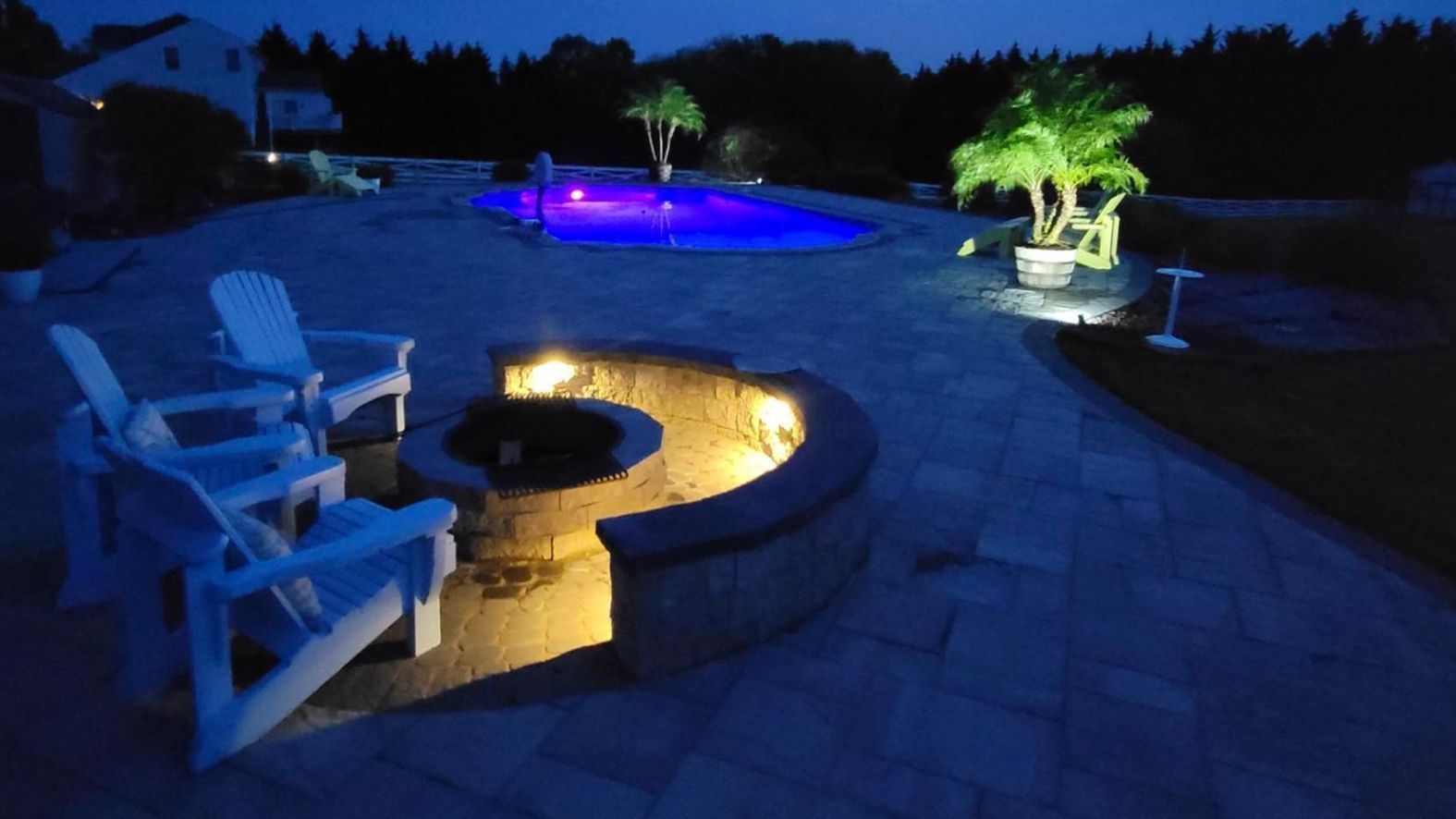 A fire pit is lit up at night next to a fiberglass pool in maryland