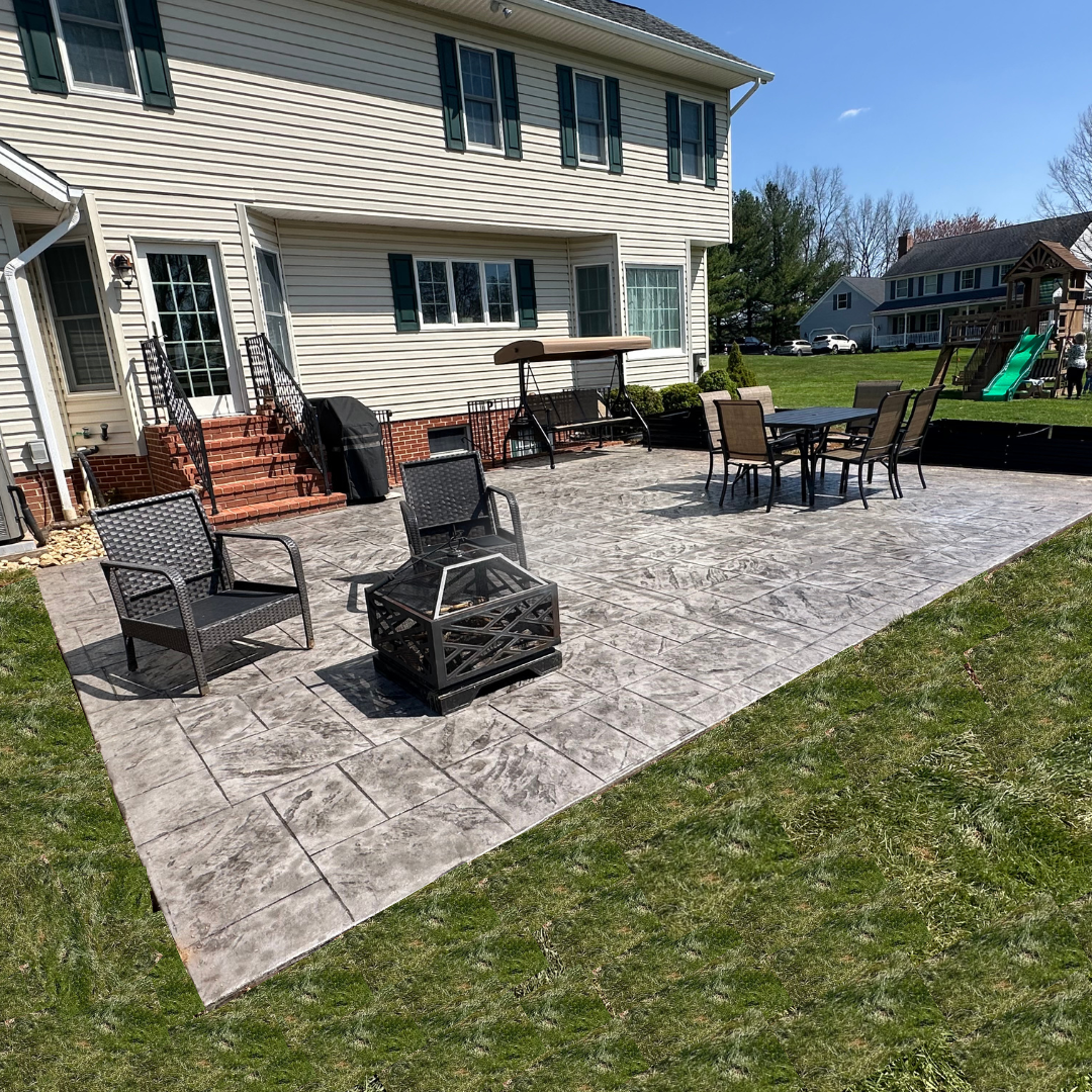A patio with a fire pit and chairs in front of a house.