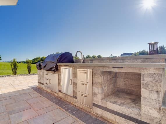 Outdoor kitchen with grill, sink, and storage cabinets under a bright blue sky.