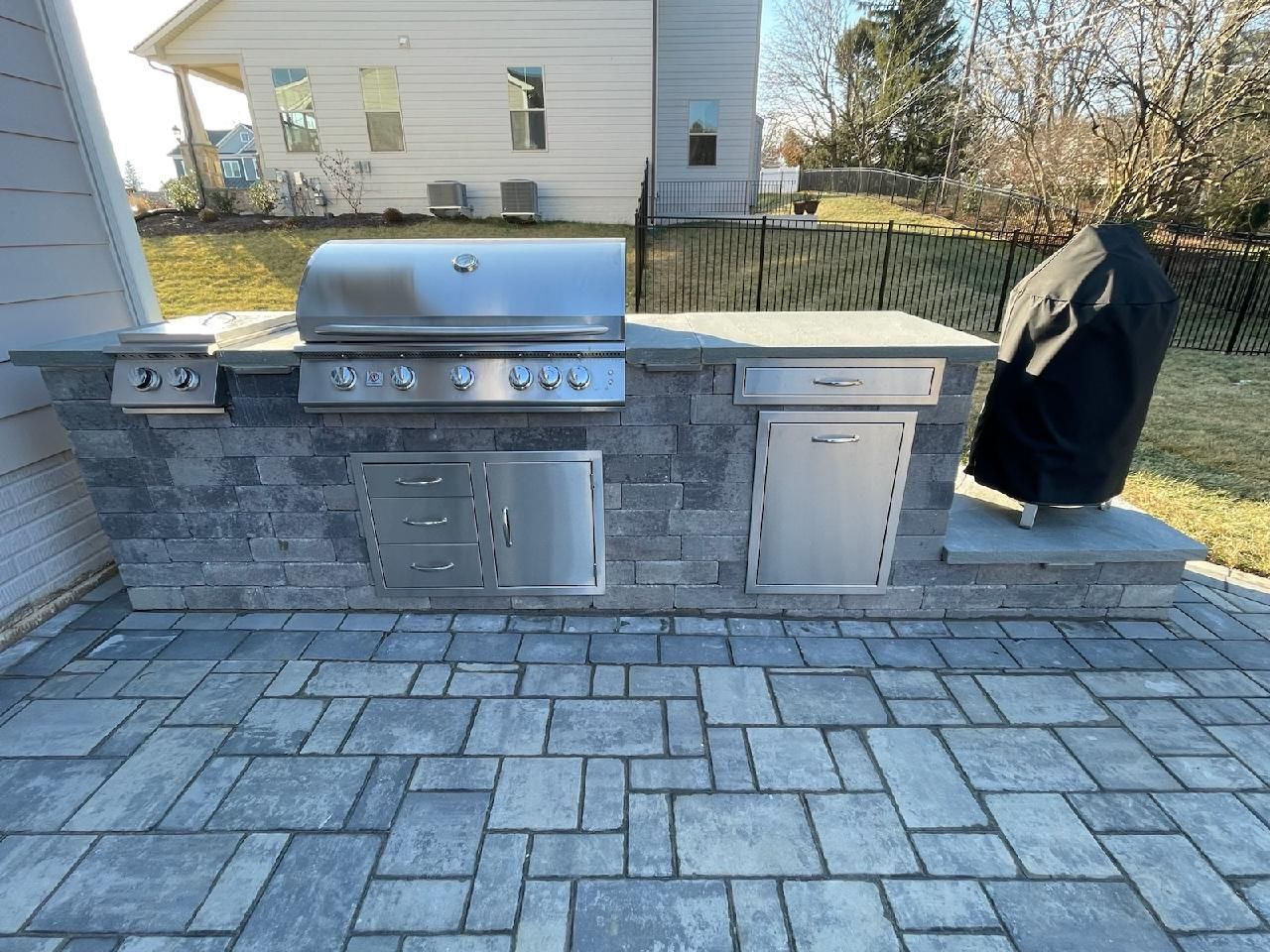 A grill is sitting on a brick patio in front of a house.