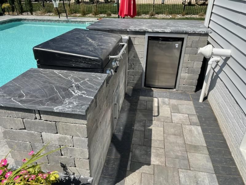 A patio with a grill and a refrigerator next to a pool.
