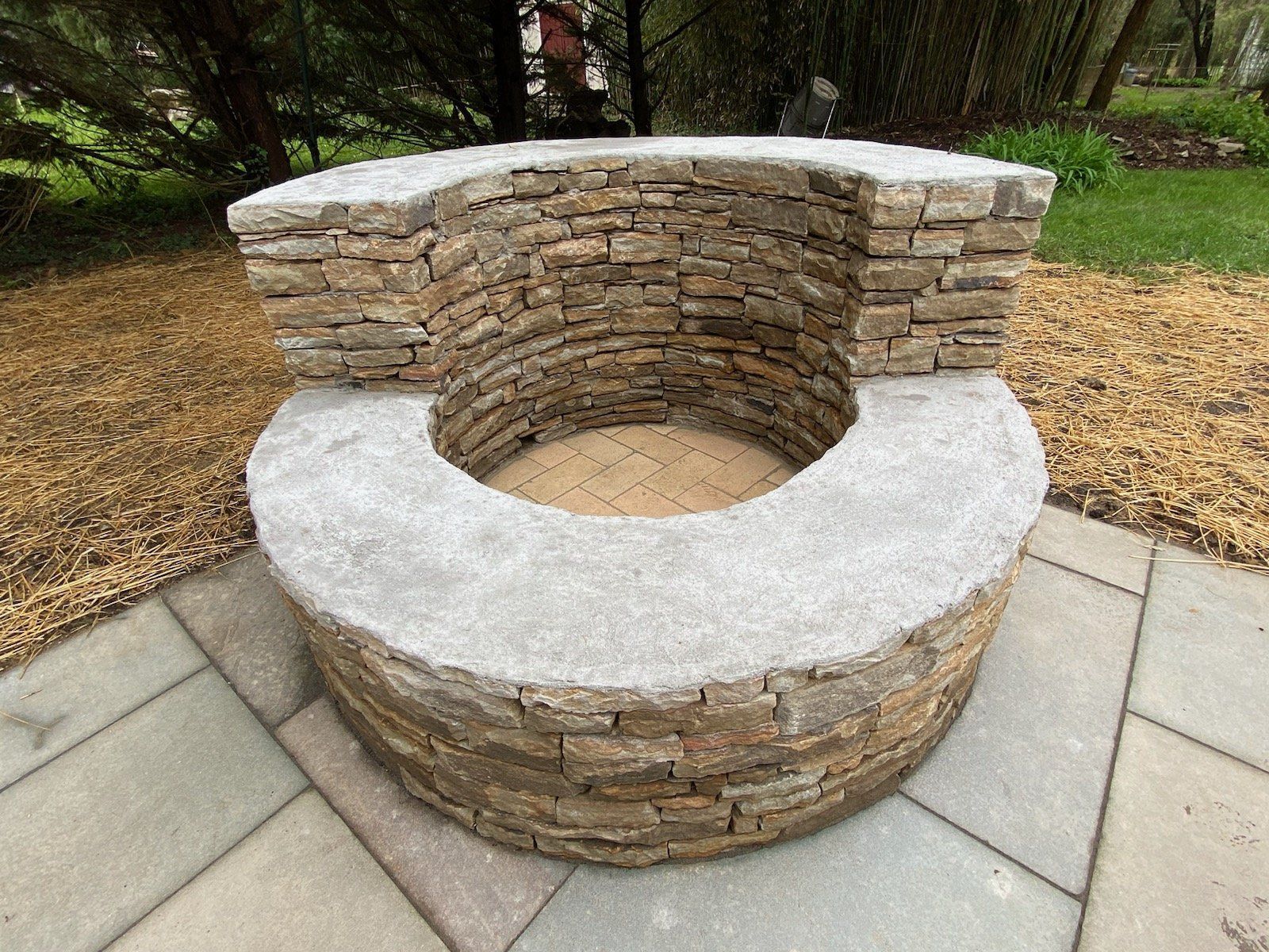 A fire pit made of stone and concrete is sitting on a patio.