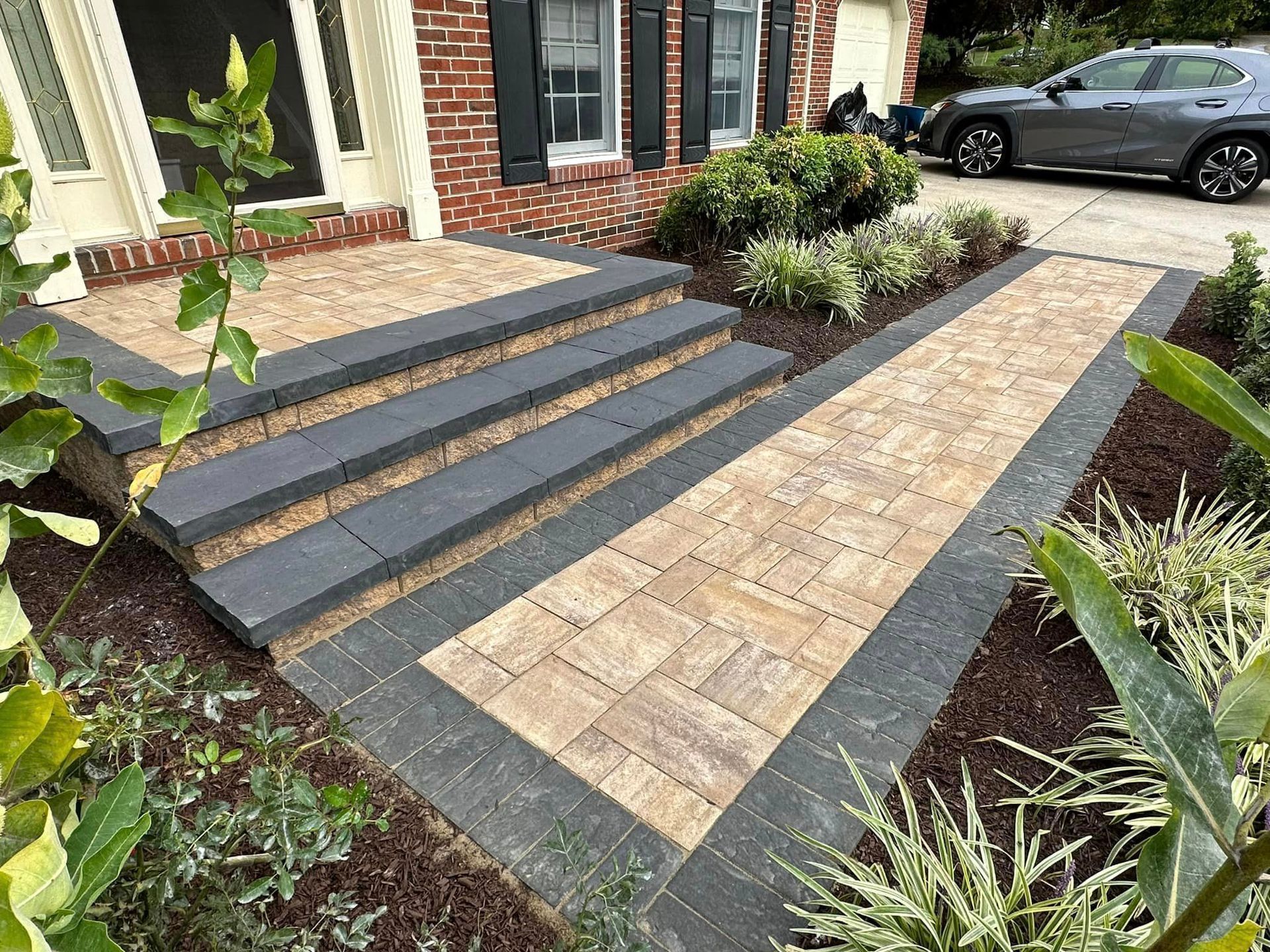 A car is parked in front of a brick house with steps and a walkway.