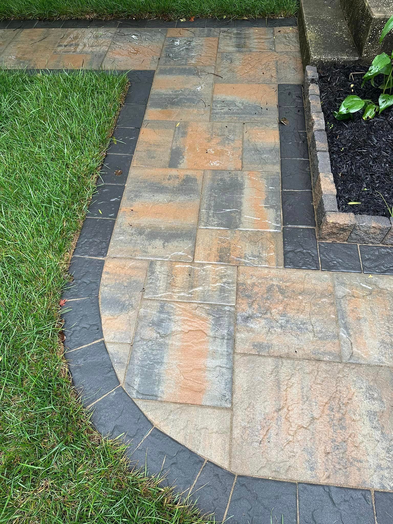 A brick walkway with a black border is surrounded by grass.