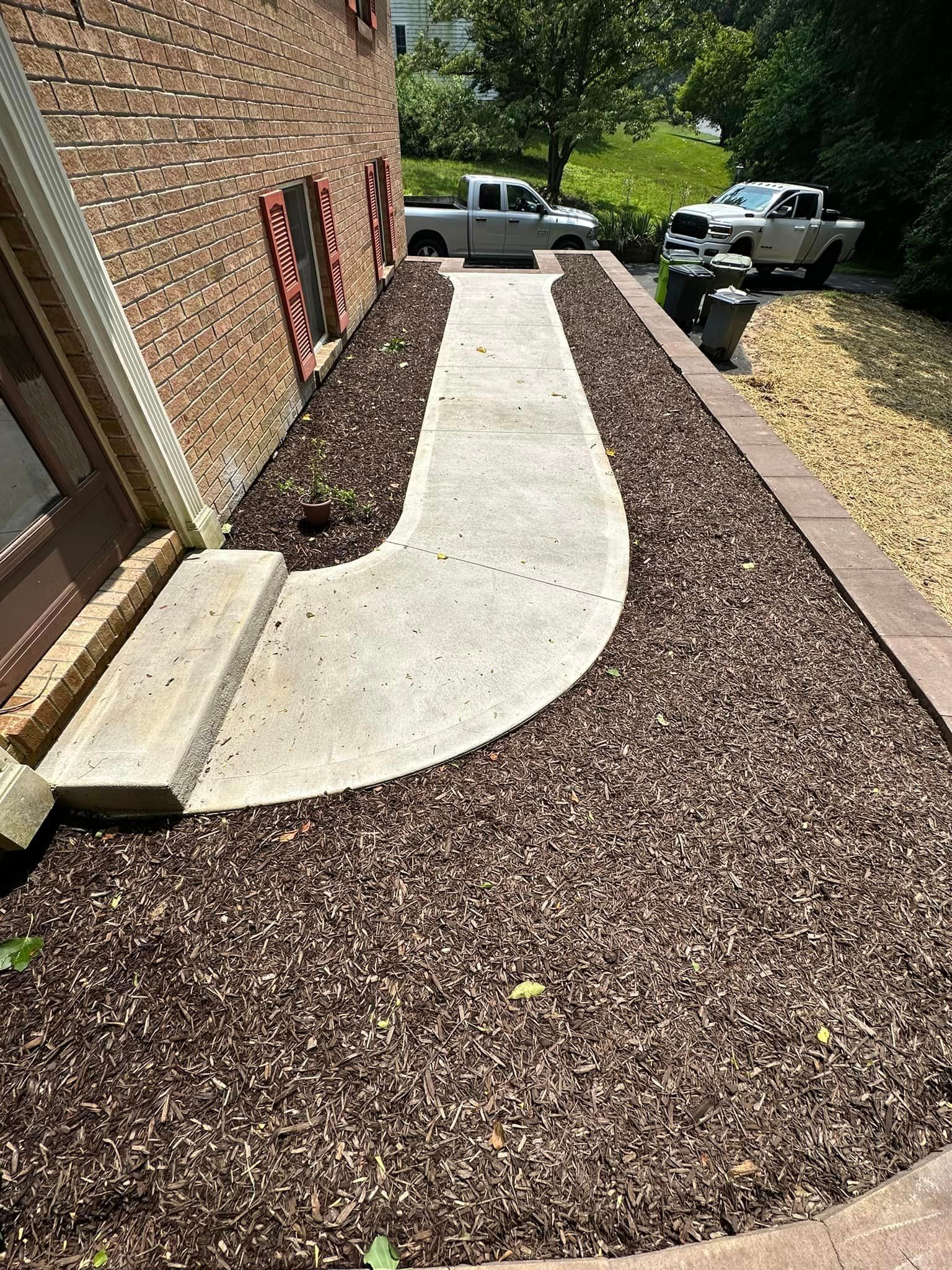 A concrete walkway surrounded by brown mulch next to a brick building.