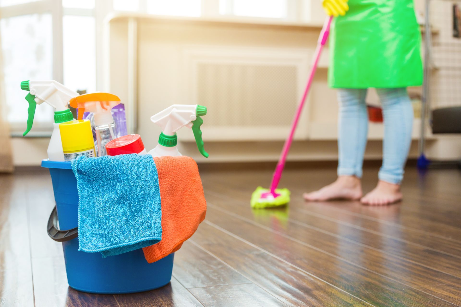 A woman is cleaning the floor with a mop and a bucket of cleaning supplies.