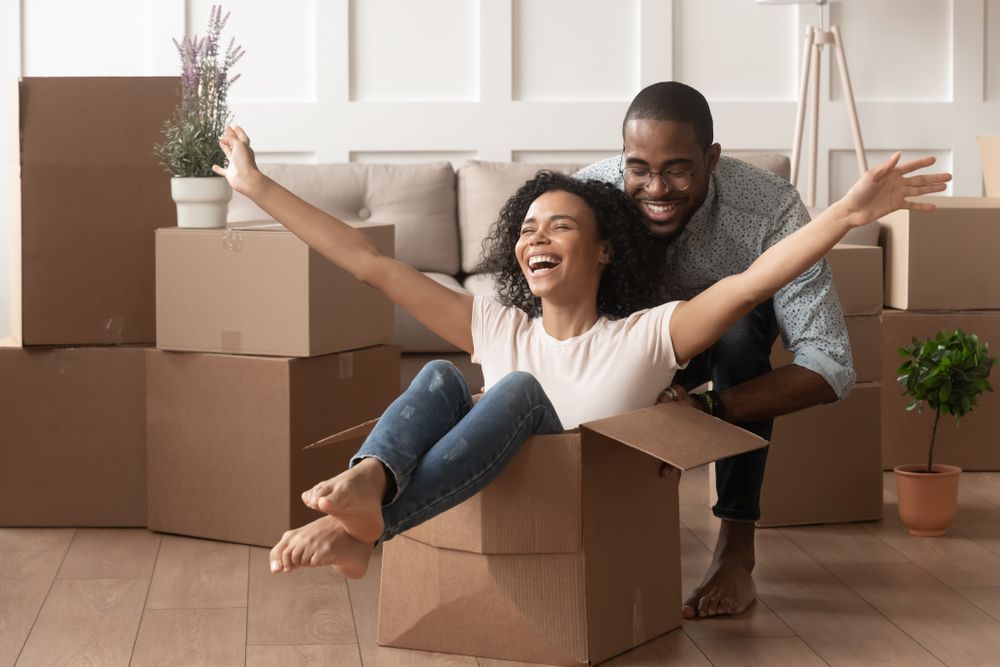 A man and a woman are sitting in a cardboard box with their arms outstretched.