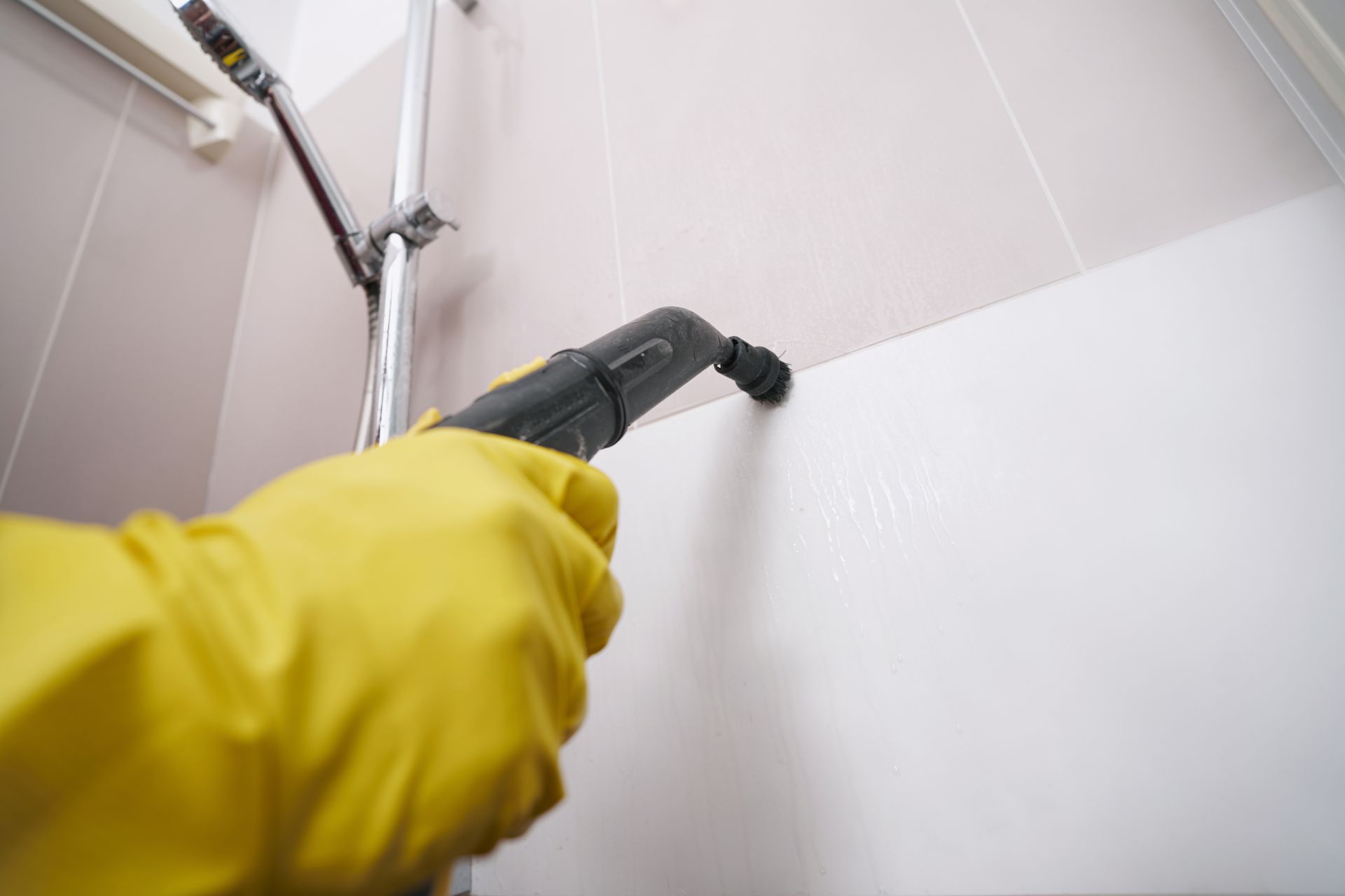 A person wearing yellow gloves is cleaning a wall with a vacuum cleaner.