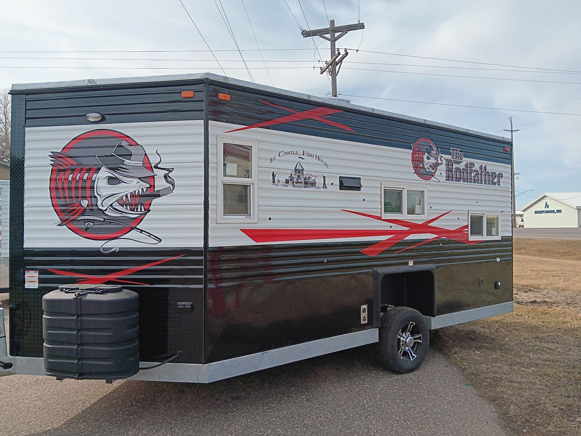 Ice fishing shack with black and red graphics, parked outdoors.