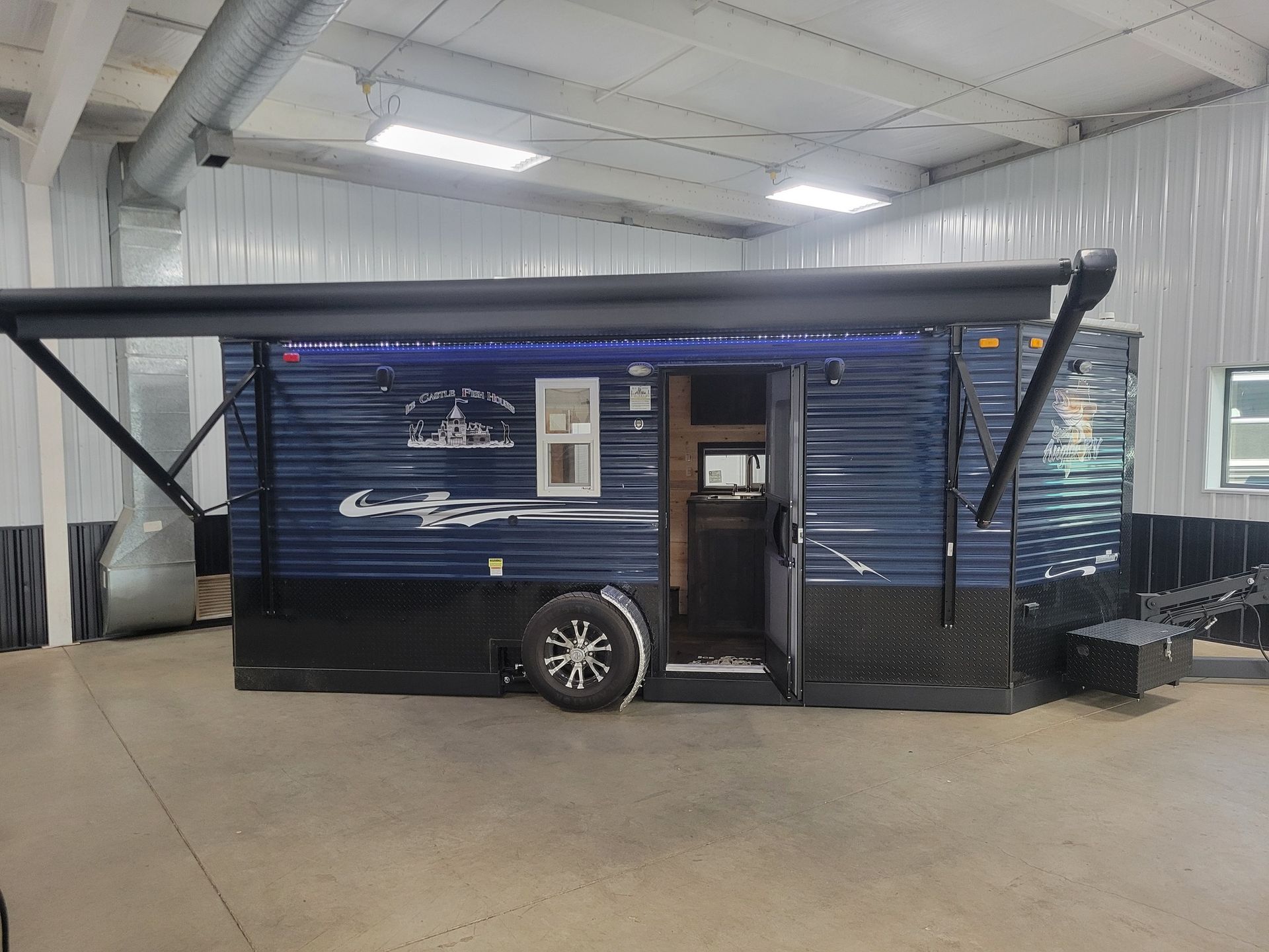 Blue ice fishing shelter with black trim and awning, in an indoor setting.