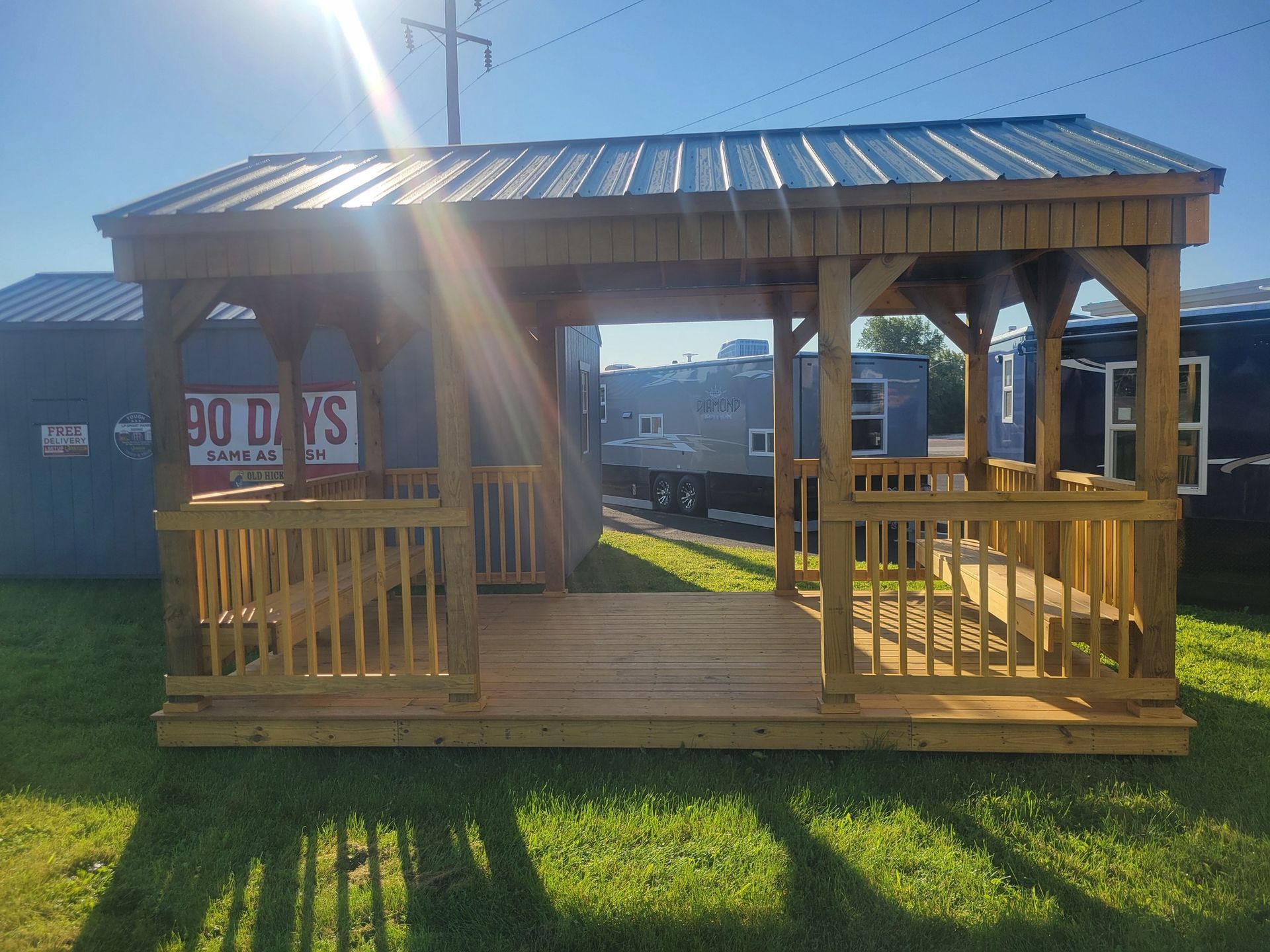 Wooden gazebo with a metal roof on grass. Sun shining.