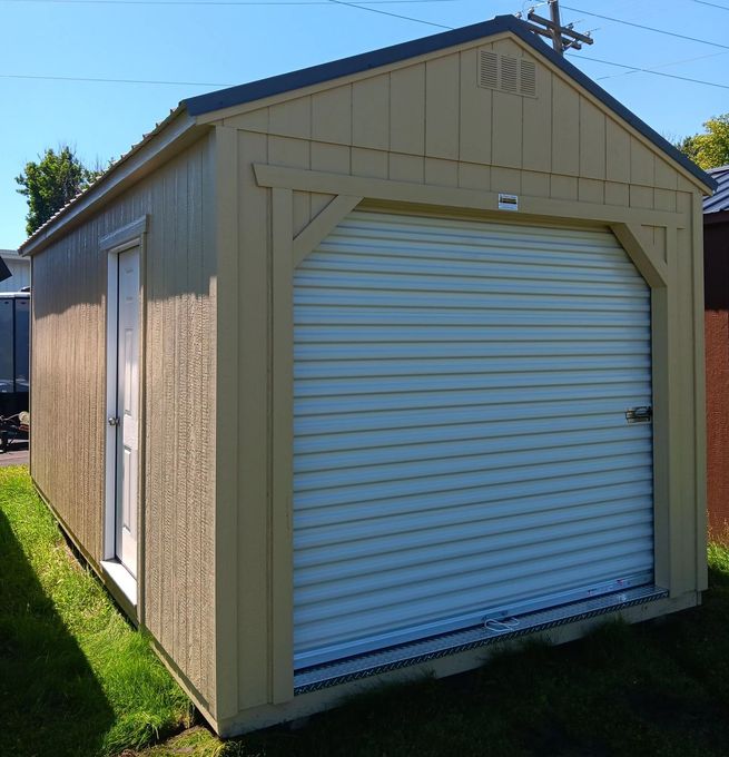 Tan shed with a roll-up garage door and a side door, set on grass, against a blue sky.