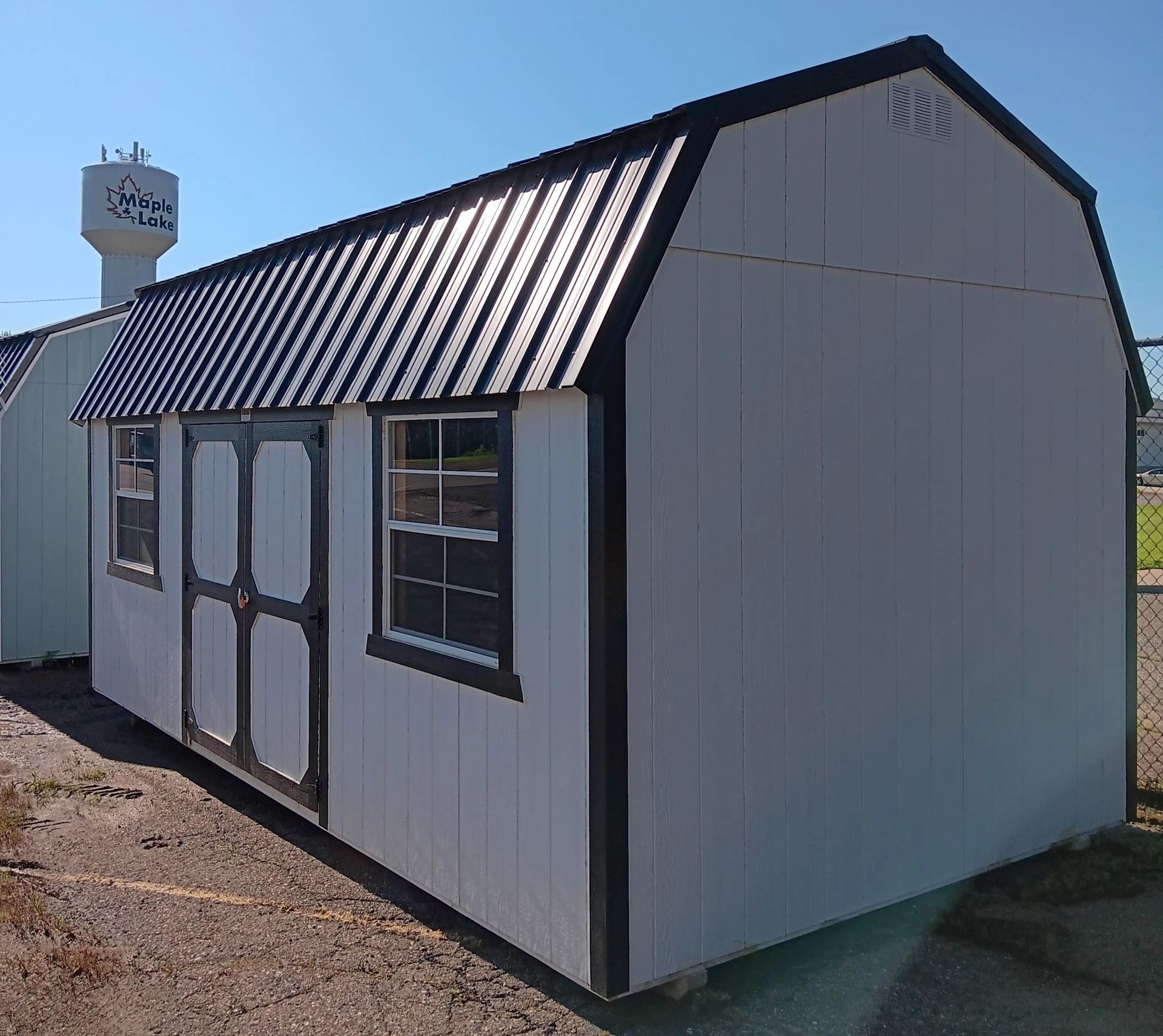 White shed with black trim, barn roof, doors, and two windows.