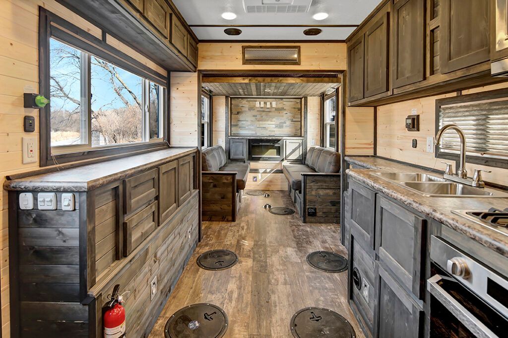 Interior of a camper with a sofa, cabinetry, window, vent, and dark flooring.