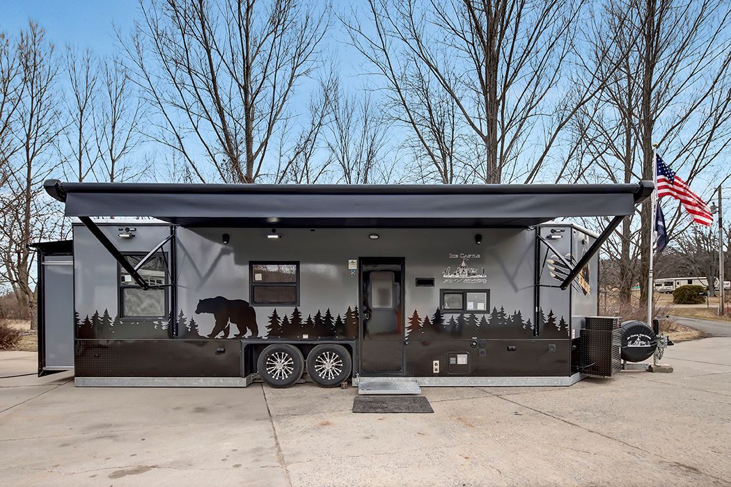 Red and black ice fishing house, windows, spare tire, logo on side, inside a garage.