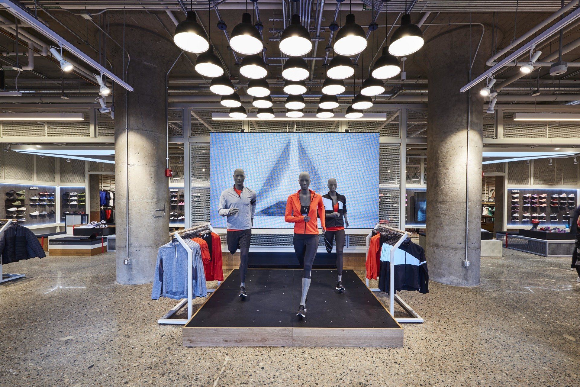 A reebok store with mannequins in front of a large screen.