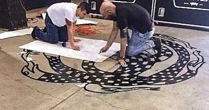 Two men are kneeling on the floor looking at a drawing on the floor.