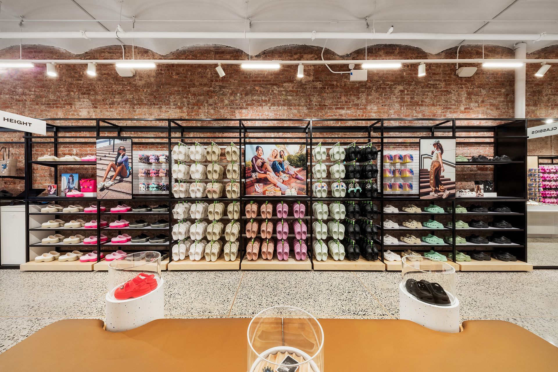 Shoe store display with colorful shoes and promotional posters against a brick wall.