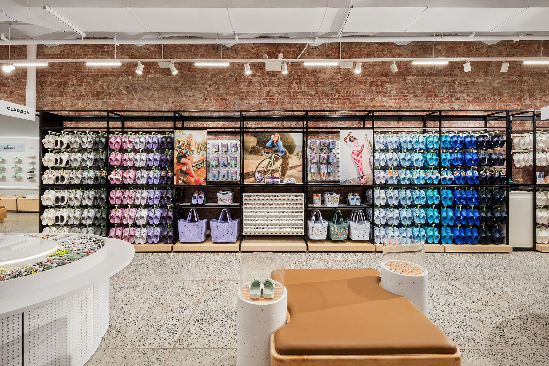 Interior shot of a shoe store with colorful shoe displays, a bench, and a brick wall.