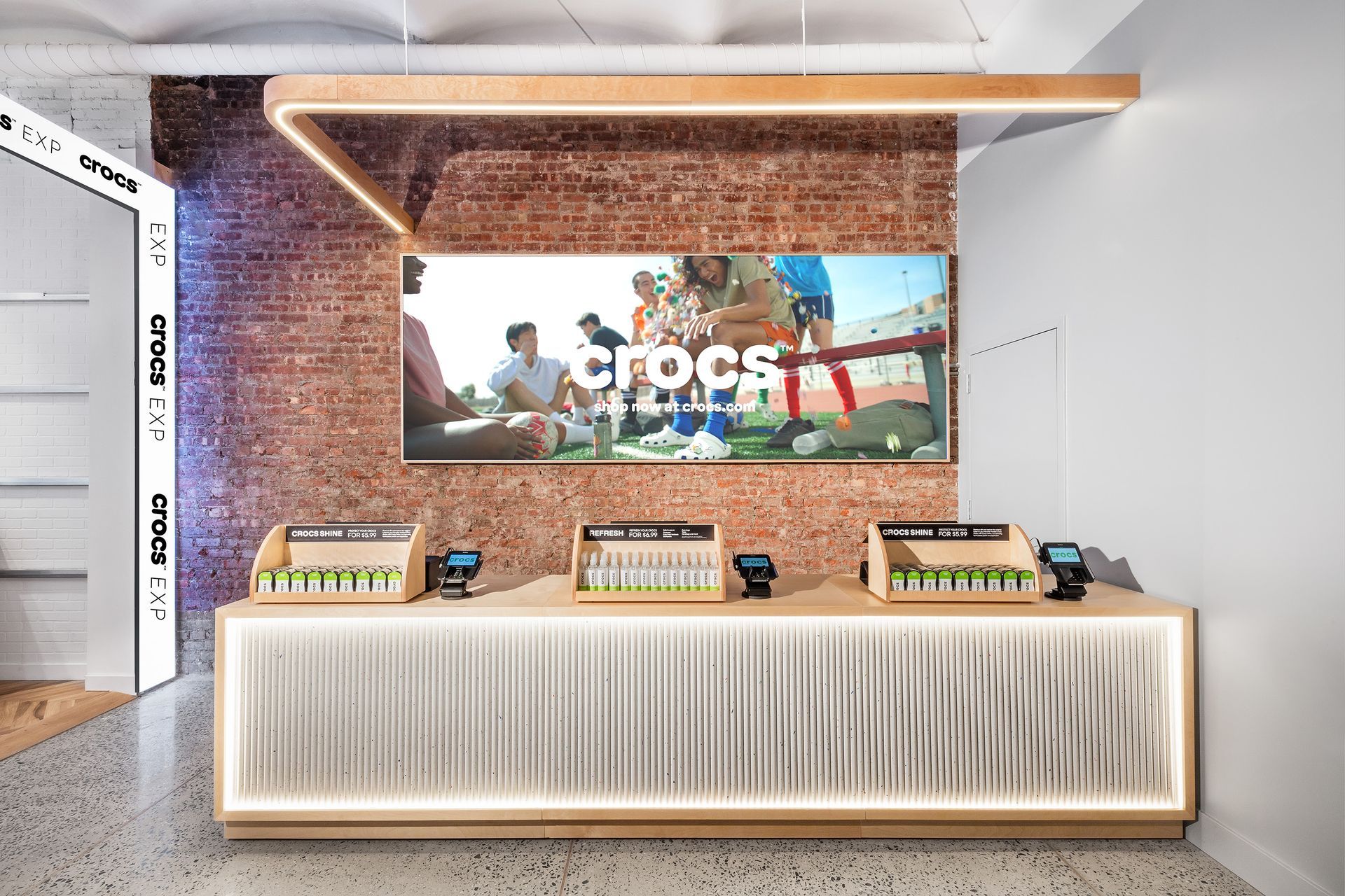 Crocs retail space with a large screen, display counters, and brick wall backdrop.