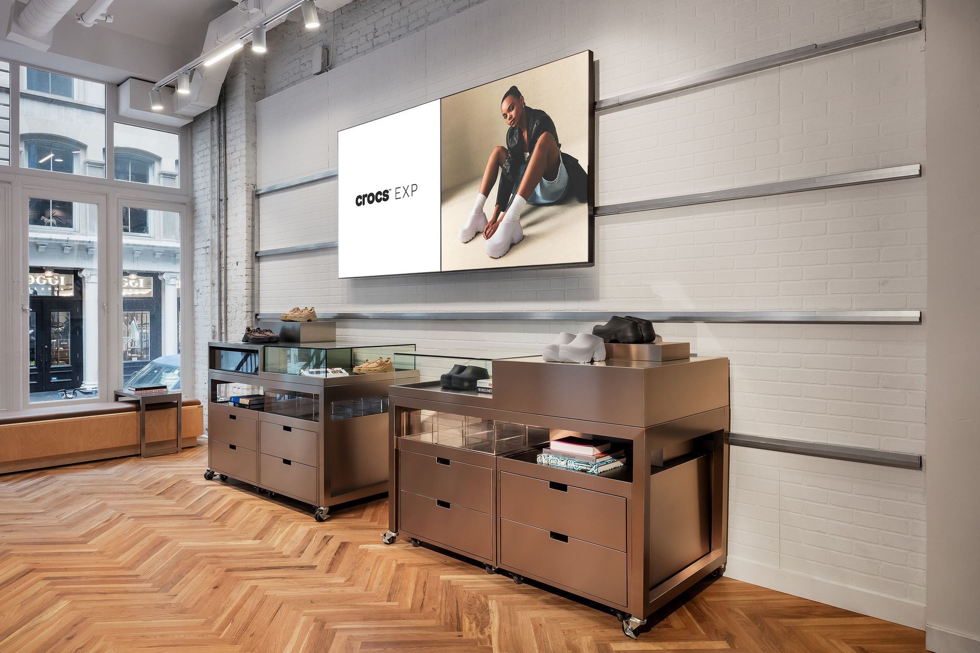 Sneaker store interior: displays, TV screen, and hardwood floors. A man on screen models shoes.