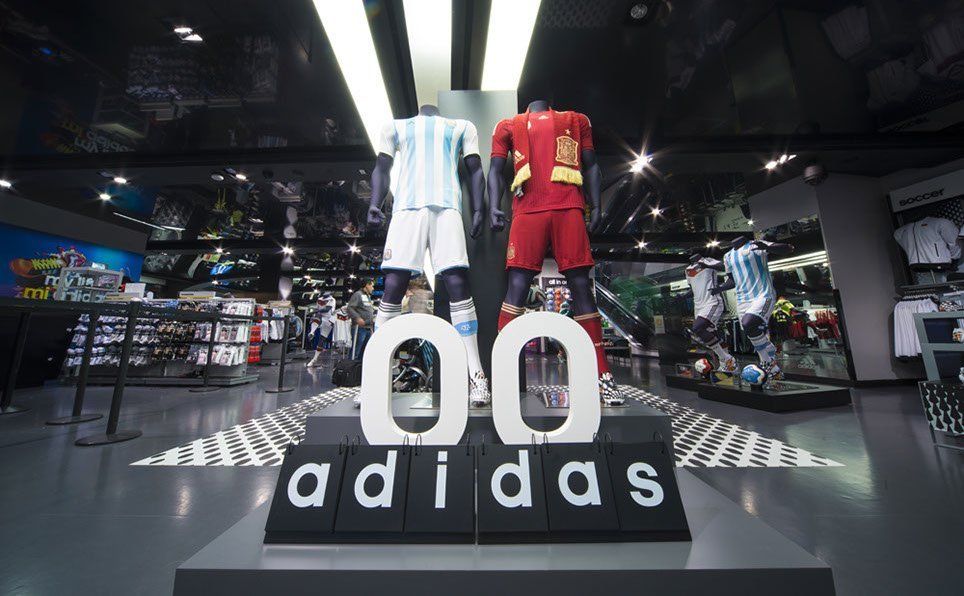 Two mannequins are standing in front of an adidas sign in a store.