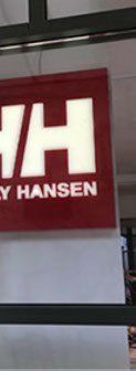 A red and white sign for helly hansen is hanging from the ceiling.