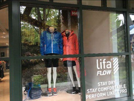 A store window with mannequins wearing jackets and shorts.