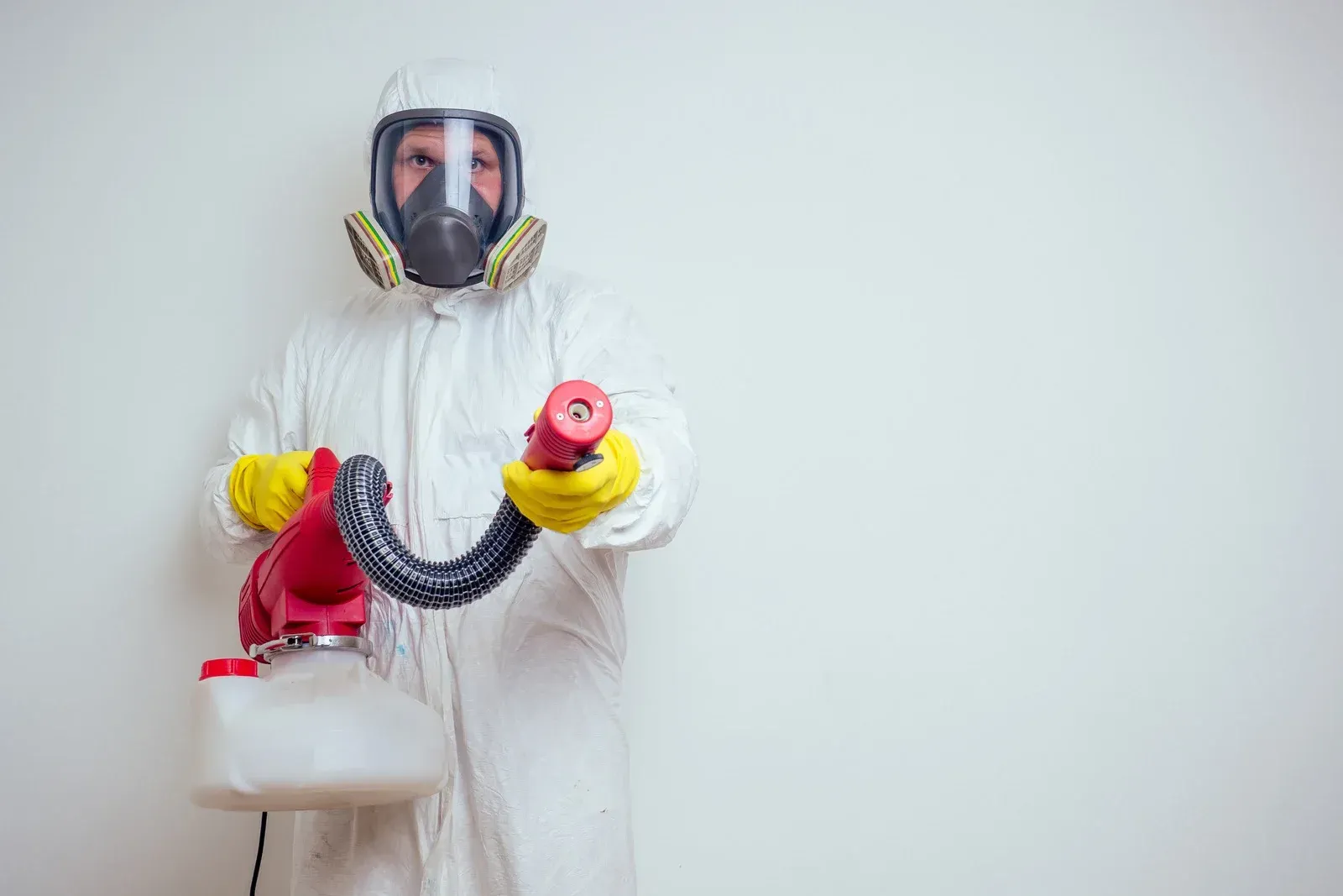 A man in a protective suit and mask is holding a sprayer.