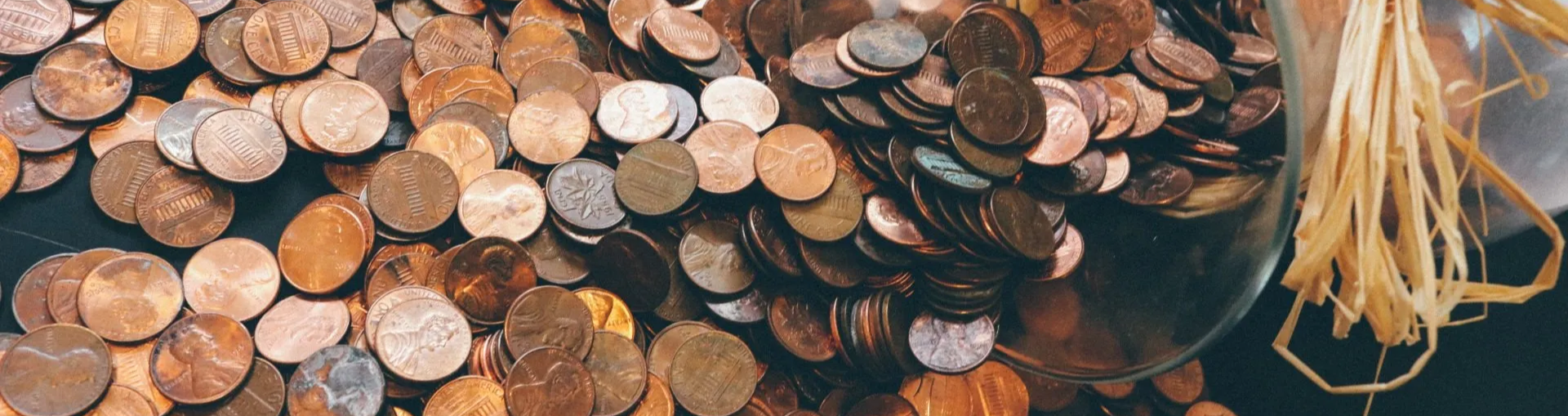 pile of u.s. pennies spilling out of a glass jar with a rustic looking bow on it