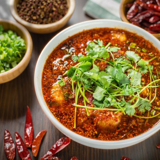 Bowl of spicy red soup topped with cilantro, surrounded by dried chilies and seasonings