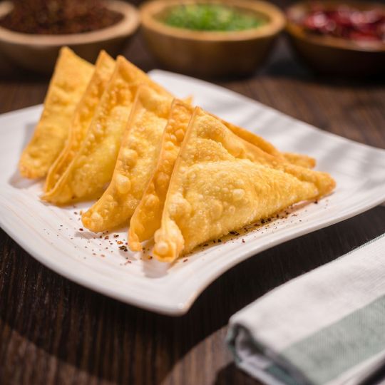 Fried triangular pastries on a white plate with dipping sauces in the background