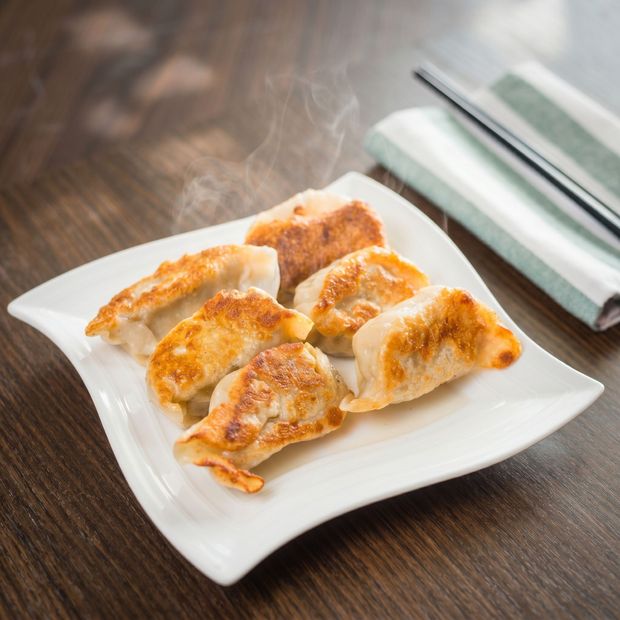 Plate of golden-brown dumplings on a wooden table with chopsticks and a folded napkin nearby