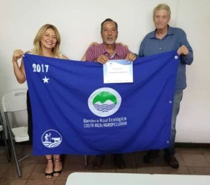 Three people hold a blue banner with a certificate in front of a plain wall.
