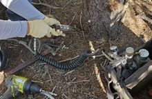 Gloved hands adjusting hoses and pressure gauges on outdoor machinery near a rocky ground