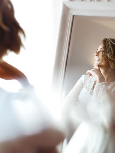 A woman in a wedding dress is looking at her reflection in a mirror.