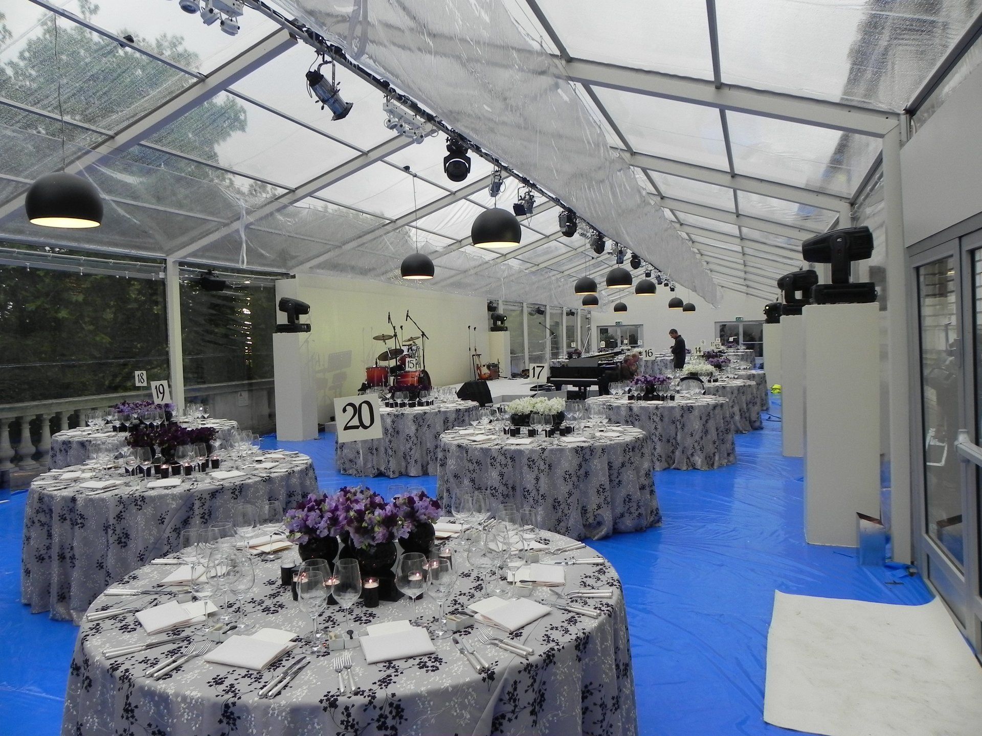 Tables with purple flowers on them are set up under a clear tent