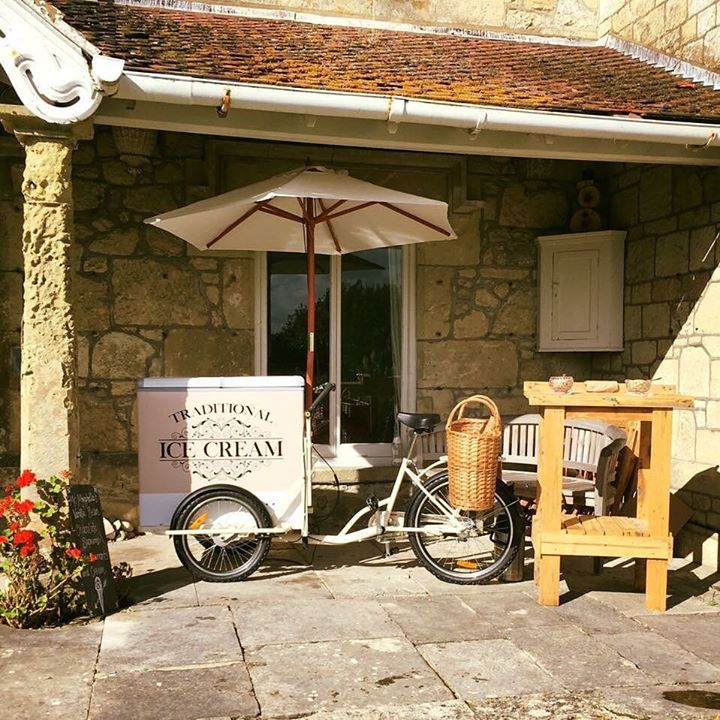 An ice cream cart is parked in front of a stone building