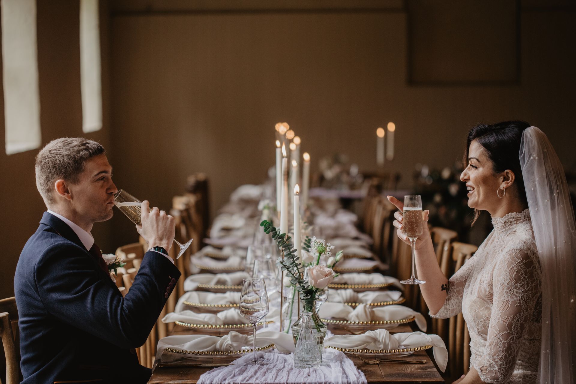 A bride and groom are sitting at a long table drinking champagne.