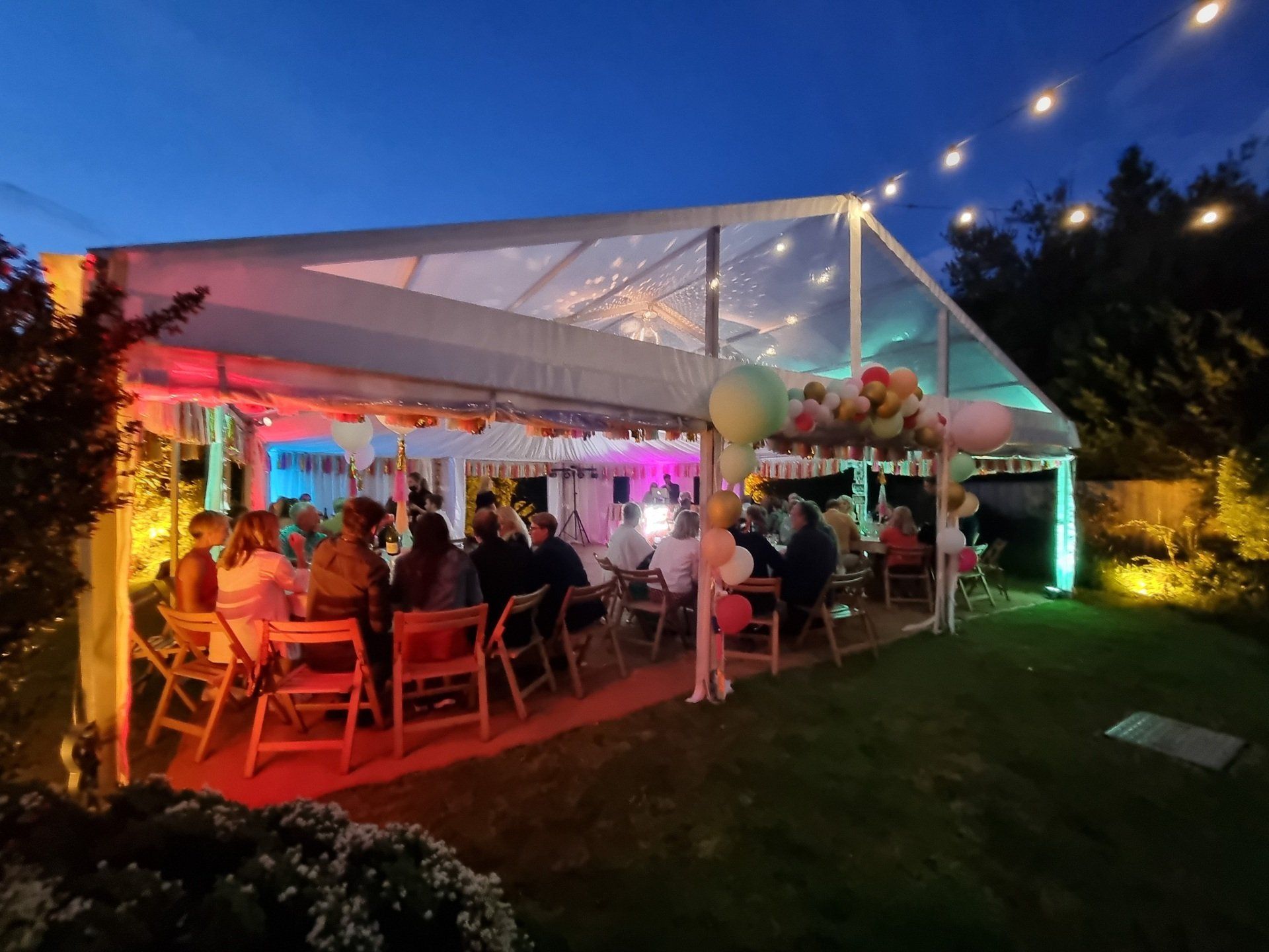 A group of people are sitting under a tent at night.