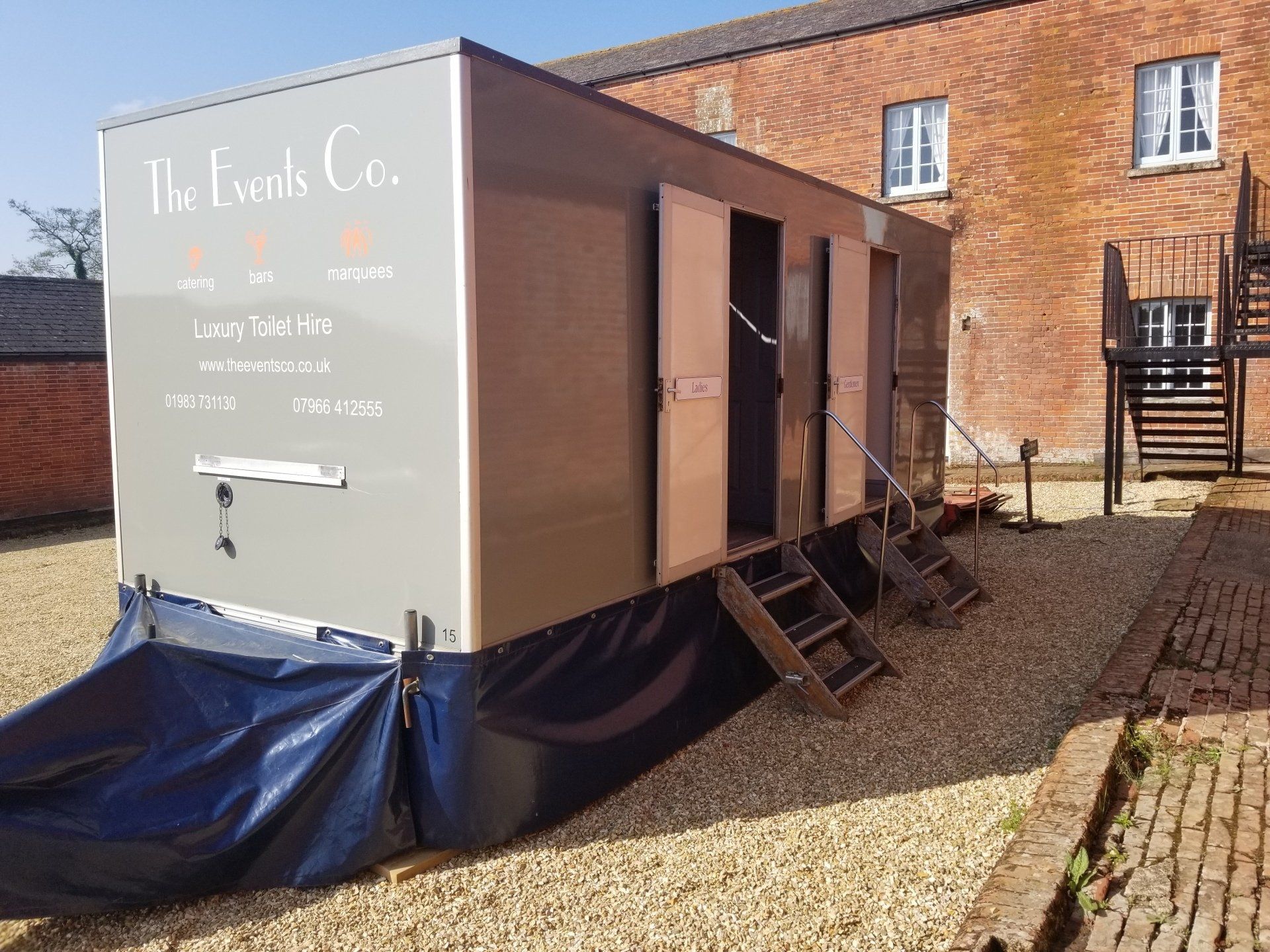A trailer is parked in a gravel lot in front of a brick building.